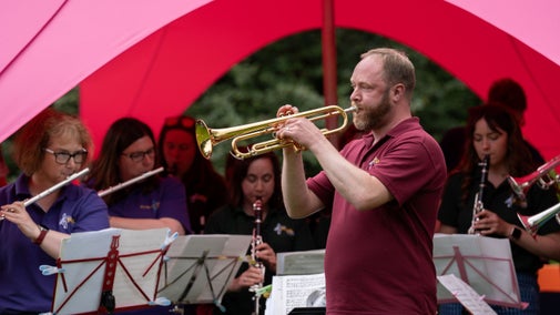 A man plays the trumpet as part of a wind band (who are seated behind him) at Tunes in the Blooms event in the Walled Garden at Wallington, Northumberland